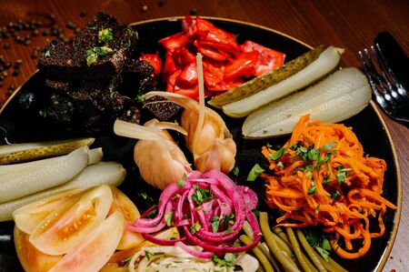 Different types of vegetables on black plate. Pickled cucumbers, tomato cherry, greens, mushrooms and garlic with onion and lettuce on the tableの写真素材