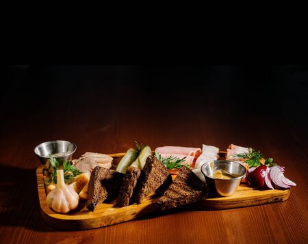 Sliced from various types of lard, ham with sauce and pickles on a wooden board. Assorted ham, lard, pickles and sauces on a wooden board.の写真素材