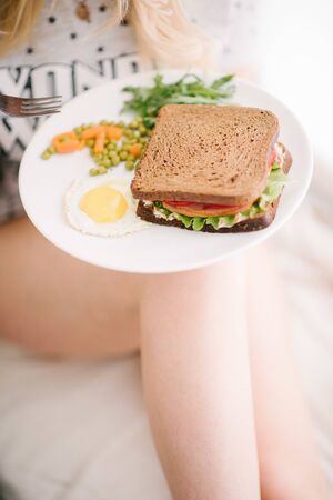 Woman holding a plate with breakfast. Fried egg and sandwich in a plate for breakfastの写真素材