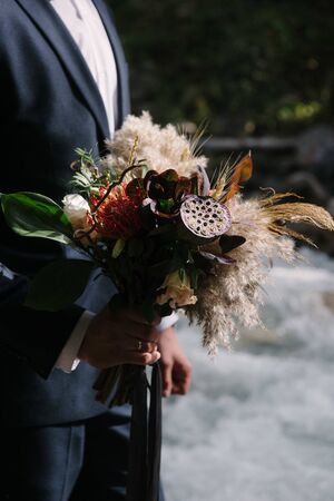 A man in a suit holds a wedding bouquet of flowersの写真素材