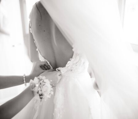 A white wedding dress is knitted to the bride. A bride is being helped to wear the wedding dress. The bride's preparation for the weddingの写真素材
