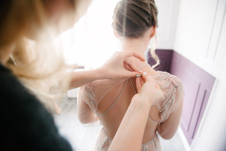 A white wedding dress is knitted to the bride. A bride is being helped to wear the wedding dress....