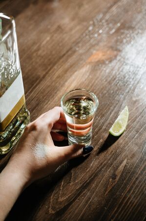 hand with tequila shots on wooden tabletop.Girl holding margarita cocktail on the table in the restaurant. Alcoholic drinks. Beautiful hands.の写真素材