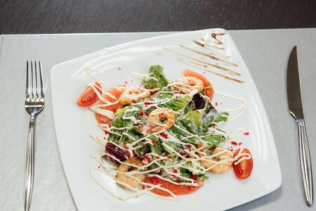 Salad with shrimps, salmon slices, tomatoes, greens on a plate on the tableの写真素材
