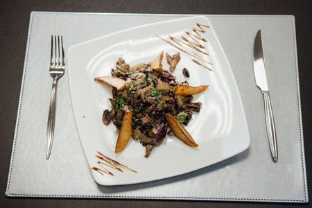 Salad with fried mushrooms, fried potatoes, greens on a plate on the table