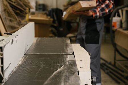 Working process in the carpentry workshop.A man in overalls uses sthicknessing planer machine in a carpentry workshop.Profession, carpentry, woodwork and people conceptの写真素材
