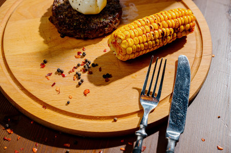 Delicious beef burger steak with spices and herbs on cutting board and slate background. Juicy fried...