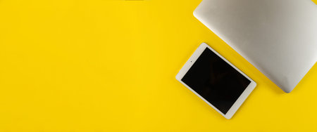 laptop and tablet on a yellow background, top view. Workplace with laptop and digital tablet on a...