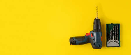cordless drill, screwdriver with drill bit on yellow background, top view. Drill with drills of different types and sizes on a yellow background, flat layの写真素材