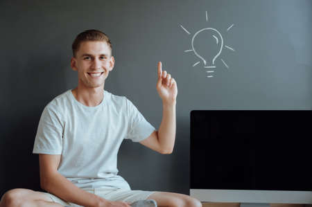 Young smiling man has an idea.Idea concept.Portrait young man has an idea, pointing with finger up on gray wall background.の写真素材