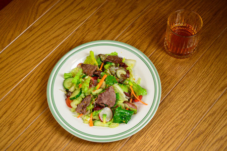 Fried meat with vegetables. Salad with meat, tomatoes, peppers, cucumbers and salad on wooden backgroundの写真素材
