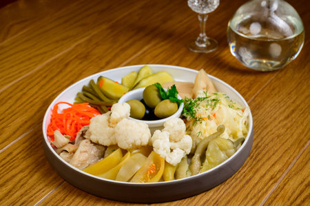 Different types of pickled vegetables on a white plate. Pickled cucumbers, tomato cherry, greens, mushrooms and garlic with onion and lettuce on the tableの写真素材