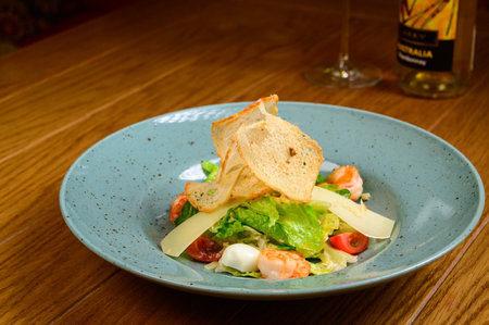 Caesar salad with shrimp on blue plate on wooden background. Caesar salad with shrimps, top viewの写真素材
