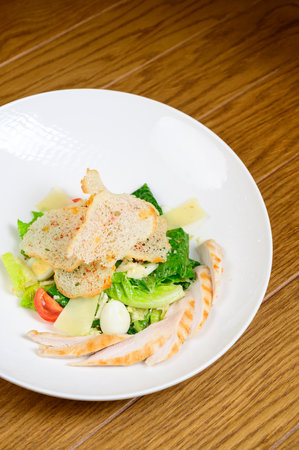 Caesar salad with croutons, quail eggs, cherry tomatoes and grilled chicken in wooden table. Delicious salad with chicken, nuts, egg and vegetables.の写真素材