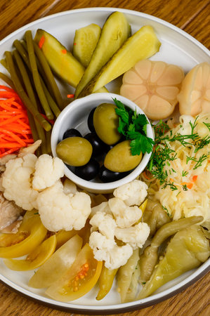 Different types of pickled vegetables on a white plate. Pickled cucumbers, tomato cherry, greens, mushrooms and garlic with onion and lettuce on the tableの写真素材
