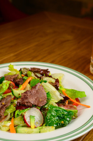 Fried meat with vegetables. Salad with meat, tomatoes, peppers, cucumbers and salad on wooden backgroundの写真素材