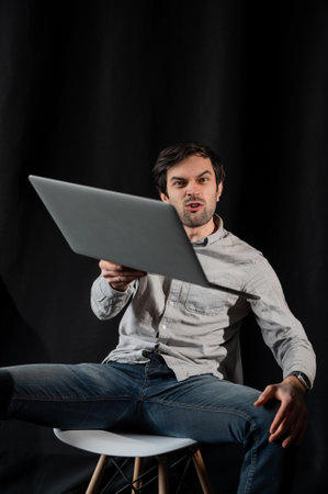 Pleasant positive business man using laptop.Happy smiling man in shirt works on laptop on a dark background.Young man working on his notebookの写真素材