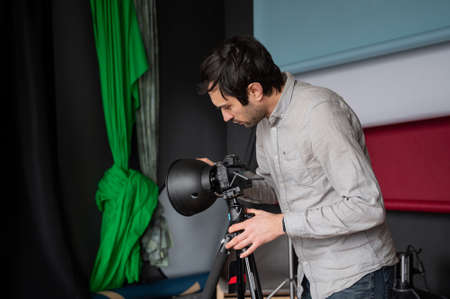 Photographer adjust softbox light intensity in studio. Man setting photographing equipment getting ready for a photo shoot.の写真素材