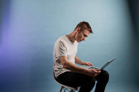Young man using laptop indoors on blue background. Young caucasian man working on laptop.A man...