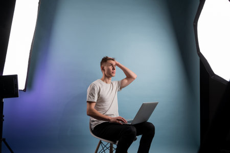 Young man using laptop indoors on blue background. Young caucasian man working on laptop.A man sitting on a chair and working on a laptopの写真素材