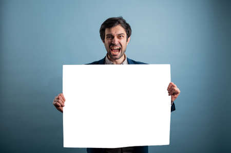 Screaming mad man holding blank poster.Screaming man holding a white poster.Angry man showing blank signboard with empty copyspace area for slogan or advertising text messageの写真素材