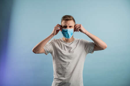 Young man tearing medical mask in studio. Removing mask, quarantine ends. Getting out of isolationの写真素材