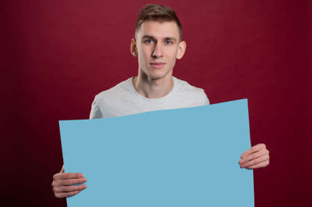 Young happy man holding a blue poster.Happy smiling young man showing blank signboard with empty copyspace area for slogan or advertising text message. Caucasian male model in advertisiment concept.の写真素材