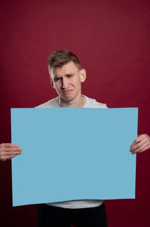 Sad young man holding blue advertising banner. Sad young man with empty advertising banner. Man holds board for advertising. Handsome man with sign board. Space for text. Advertising. Black friday.の写真素材