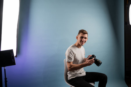 Handsome young photographer using camera on blue background.Man using a professional camera.Portrait of guy looking at photo cameraの写真素材