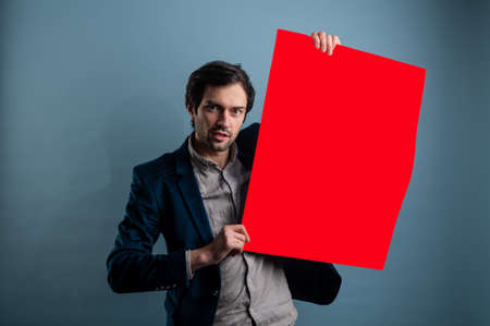 Happy man holding a red poster.Happy smiling young man showing blank signboard with empty copyspace area for slogan or advertising text message. Caucasian male model in advertisiment concept.の写真素材