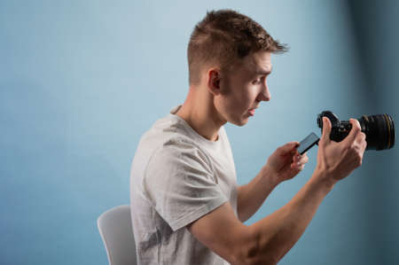 Handsome young photographer using camera on blue background.Man using a professional camera.Portrait of guy looking at photo cameraの写真素材
