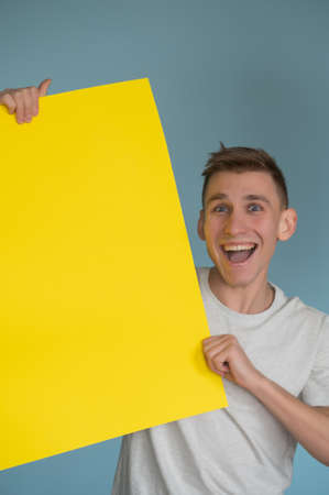 Young happy man holding a yellow poster.Happy smiling young man showing blank signboard with empty copyspace area for slogan or advertising text message. Caucasian male model in advertisiment concept.の写真素材