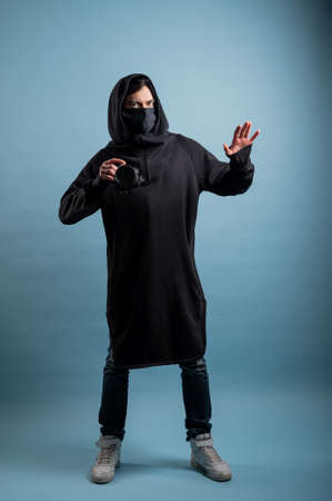 Portrait of positive photographer, man with medical mask holding professional digital dslr camera. Indoor studio shot isolated on blue background. The photographer is wearing a medical mask.の写真素材