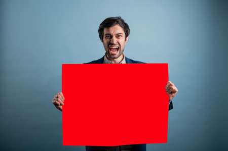 Screaming mad man holding blank poster.Screaming man holding a red poster.Angry man showing blank signboard with empty copyspace area for slogan or advertising text messageの写真素材
