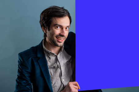 Happy man holding a blue poster.Happy smiling young man showing blank signboard with empty copyspace area for slogan or advertising text message. Caucasian male model in advertisiment concept.の写真素材