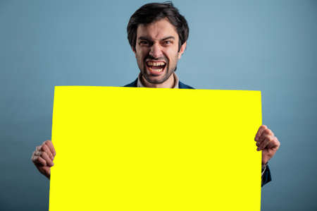 Screaming mad man holding blank poster.Screaming man holding a yellow poster.Angry man showing blank signboard with empty copyspace area for slogan or advertising text messageの写真素材
