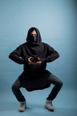 Portrait of positive photographer, man with medical mask holding professional digital dslr camera. Indoor studio shot isolated on blue background. The photographer is wearing a medical mask.の写真素材