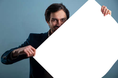 Happy man holding a white poster.Happy smiling young man showing blank signboard with empty copyspace area for slogan or advertising text message. Caucasian male model in advertisiment concept.の写真素材