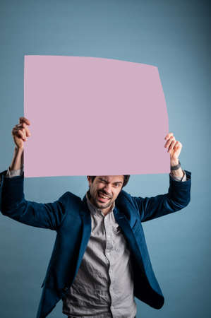 Happy man holding a pink poster.Happy smiling young man showing blank signboard with empty copyspace area for slogan or advertising text message. Caucasian male model in advertisiment concept.の写真素材