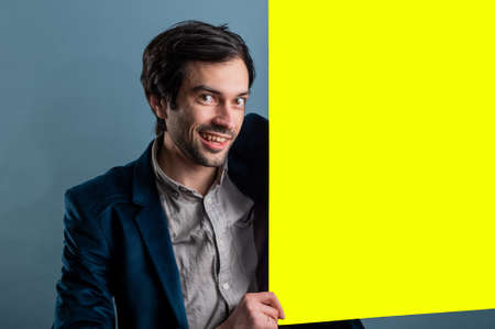 Happy man holding a yellow poster.Happy smiling young man showing blank signboard with empty copyspace area for slogan or advertising text message. Caucasian male model in advertisiment concept.の写真素材