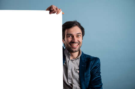 Happy man holding a white poster.Happy smiling young man showing blank signboard with empty copyspace area for slogan or advertising text message. Caucasian male model in advertisiment concept.の写真素材