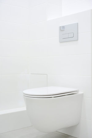 Contemporary wall-mounted toilet positioned in a minimalist bathroom featuring white tiles and a...