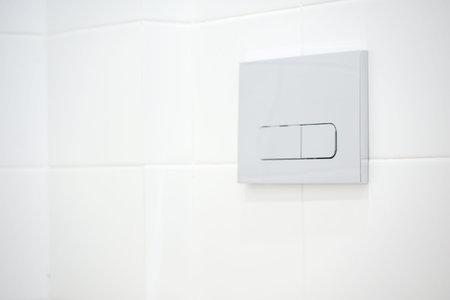 Dual flush toilet button installed on a white tiled wall, showcasing a sleek design and modern...