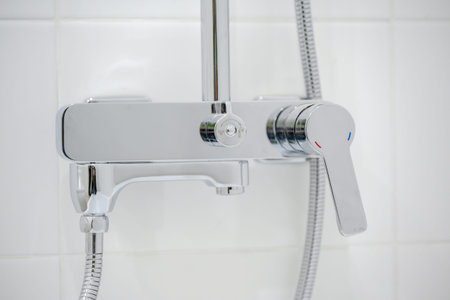 Close-up of a chrome shower faucet featuring an adjustable handle and a flexible hose attachment, mounted on a white tiled wallの写真素材