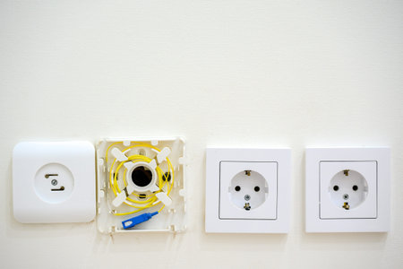 Three electrical wall sockets and an installation component are visible on a white wall, showing...
