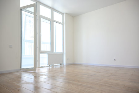Spacious empty room featuring large windows that allow natural light, wooden flooring, and a...