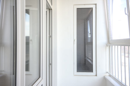 Bright, modern balcony featuring large glass windows and white walls, showing a minimalist design with a clean and spacious appearanceの写真素材