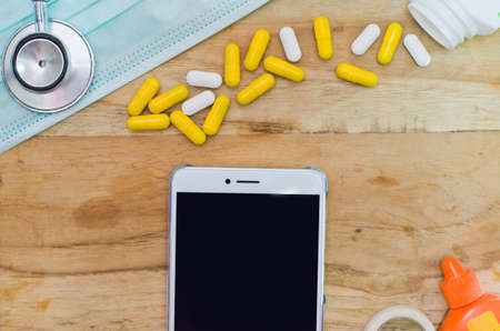 Capsule of herbal medicine with mask,old stethoscope ,Povidone-iodine, White Smart phone on wooden table background, copy spaceの写真素材