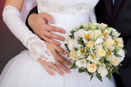 Bride and groom hands with wedding rings and bouquet of roses の写真素材