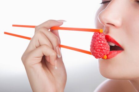 The sexy girl holds chopsticks a raspberry near lipsの写真素材